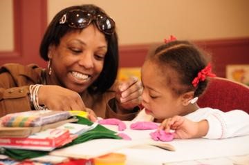 Photo of an African-American mother and her young daughter enjoying a sensory reading activity together.